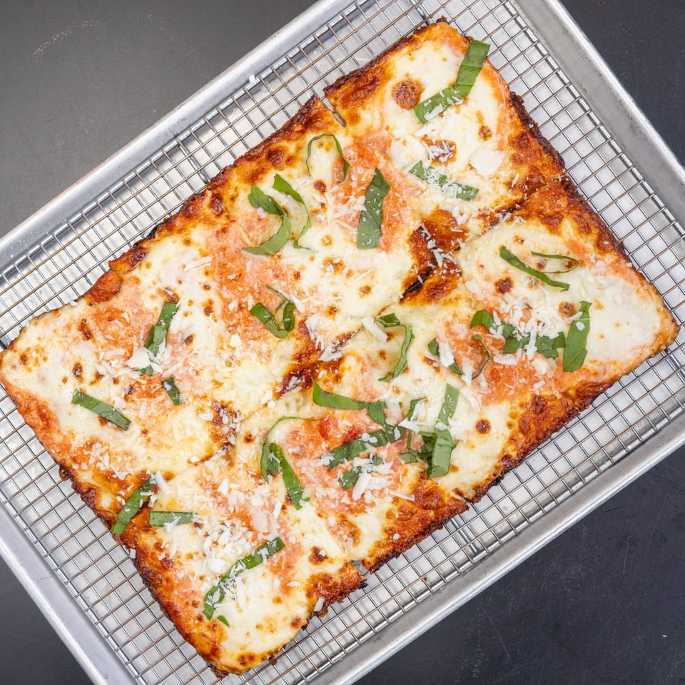 A rectangular Detroit-style pizza with melted cheese, red sauce, fresh basil, and grated parmesan.