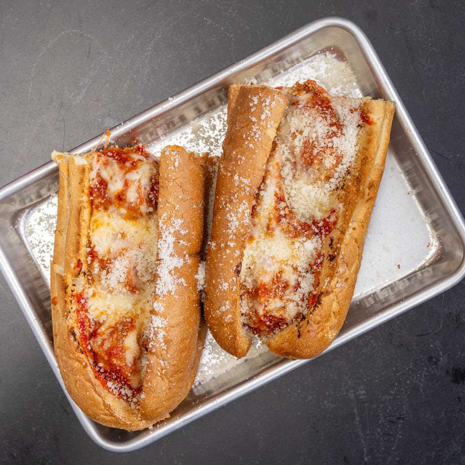 Two Detroit Pizza Co. meatball subs with melted cheese and sauce on a metal tray.