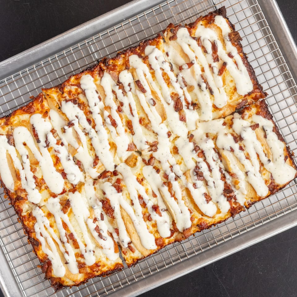 Detroit-style pizza with white sauce and bacon crumbles on a cooling rack.
