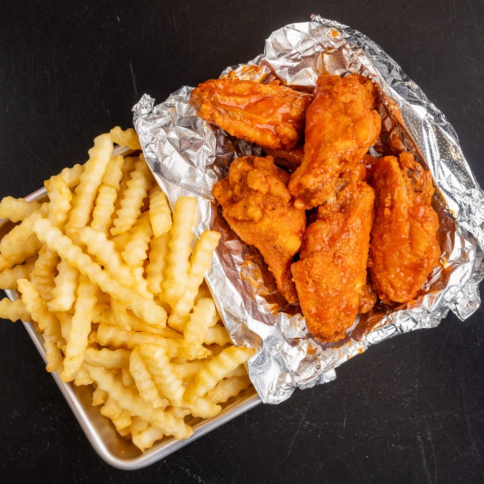 Detroit Pizza Co. buffalo wings in foil with crinkle-cut fries on a metal tray.