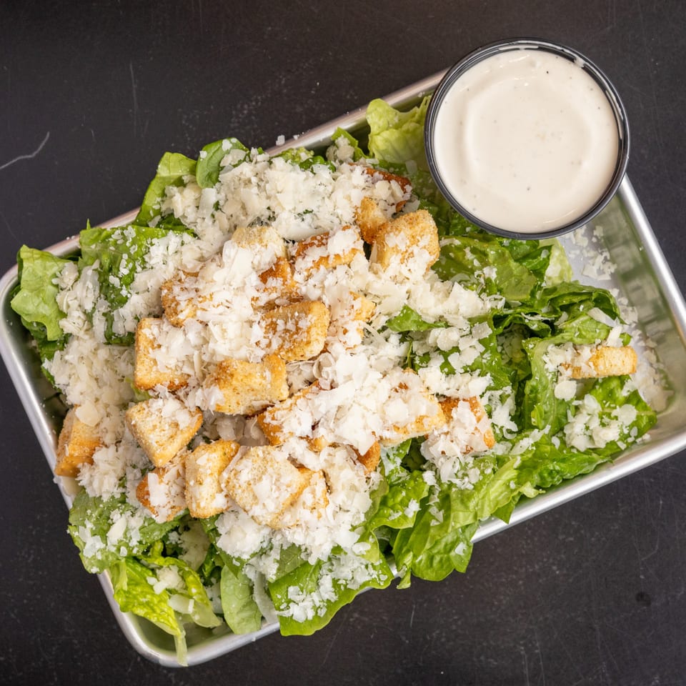 Caesar salad with romaine lettuce, croutons, parmesan cheese, and a side of dressing.